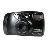 A black Pentax IQZ Zoom EZY compact instant camera with a textured white surface background.