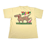 A pale yellow short-sleeve t-shirt laid flat on a light gray background, featuring a colorful graphic on the back with a cartoon dog, cat, and the words 'WAMBO DOG EAT DOG'.