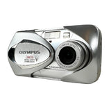 An Olympus D-580 digital camera in silver, photographed from a side angle on a light gray textured surface.