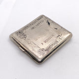 A vintage silver-toned metal cigarette case featuring an engraved United States 50 cents postage stamp design, shown on a white textured fabric background.