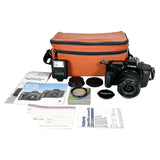 A Canon EOS 650 SLR camera with a zoom lens, shown with its accessories including an orange carrying case, a speedlight flash, filters, lens caps, manuals, and a warranty card on a white studio background.