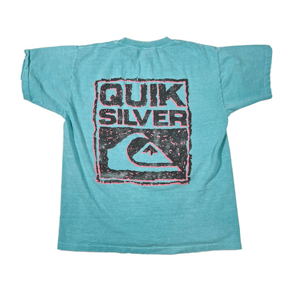 A vintage turquoise short-sleeve t-shirt laid flat on a white background, featuring a large distressed black and pink graphic on the back with the text 'QUIK SILVER' and a wave logo.