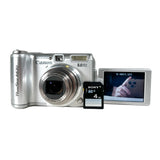 A silver Canon PowerShot A630 compact camera with its lens extended, shown next to a 4GB Sony SD memory card and a small flip-out display screen on a white background.