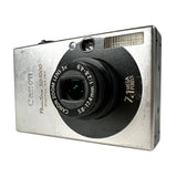 A Canon PowerShot SD1000 digital camera in silver and black, photographed at an angle on a light gray textured surface.