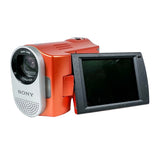 A Sony video camera with a bright orange-red body, silver lens housing, and a black flip-out screen, photographed on a white studio background.