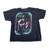A black short-sleeve graphic t-shirt featuring a large front print of Nod Cryde holding a microphone, with stylized text reading 'NOD CRYDE' in a distressed green and white font.