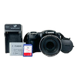 Canon SX500 IS compact digital camera with black lens cap, shown with a Canon battery charger, battery pack, and SD card on a white background.
