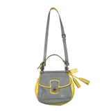 A small gray leather shoulder bag with bright yellow trim, a top handle, a long shoulder strap, and a tassel charm, photographed against a plain white background.