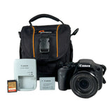 Canon DSLR camera with a zoom lens, shown with a black and orange camera bag, a Canon battery charger, a Canon battery, an SD card, and a memory card on a light gray background.