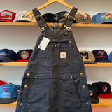 Black overalls with a Carhartt logo on a hanger against a background of hats.