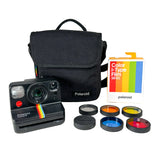 A vintage Polaroid Instant Mini camera in black with its iconic rainbow strap, shown with a black fabric carrying case, a box of Polaroid Color-Form Film 16mm, and six interchangeable film lenses on a light gray background.