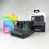 A Polaroid instant camera shown in front of its retail box, with a colorful Polaroid Color i-Type Film box standing to the left, all on a light gray studio background.