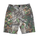 A pair of men's camouflage shorts featuring a realistic woodland print with branches, leaves, and pine needles in shades of brown, green, gray, and beige, laid flat against a white background.