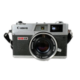A vintage Canon SLR camera with a silver and black textured body, featuring a 60mm 1:1.7 lens and a black strap, photographed against a plain light background.