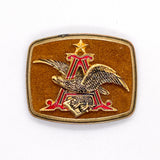 A vintage military belt buckle featuring a gold-toned eagle over a red and gold letter 'A' emblem with a star on a textured brown background.