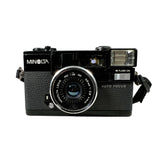 A vintage Minolta camera with a black textured body, silver lens ring, and attached flash, photographed against a plain white background.