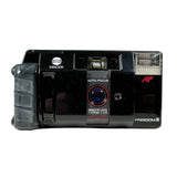 A black Minolta Freedom III AF film camera with a textured grip on the left and a clear flash cover on the right, photographed against a light gray background.