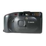 A Canon film camera in dark gray, photographed from the front on a light gray textured background.