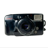 An Olympus Zoom-Lik zoom lens camera in glossy black, photographed from the front against a light gray background.