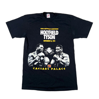A black short-sleeve graphic t-shirt laid flat on a white background. The front features a white and yellow print of boxer Holyfield Tyson at Caesars Palace on November 8, 1991.