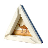 A triangular ceramic ashtray with a cream-colored body, blue striped edges, and a small central illustration of a camel on a sandy desert scene.