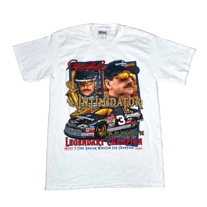 A white short-sleeve graphic T-shirt laid flat on a light gray background. The shirt features a large front print with portraits of Dale Earnhardt, the number 3 race car, and text reading 'Intimidator' and 'Legendary Champion.