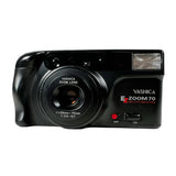 A black Yashica E-Zoom 70 compact film camera with a red eye reduction feature, shown from the front on a light gray background.