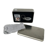 A vintage Zippo lighter with a Beatles collectible charm, shown with its original presentation tin, a gray microfiber cloth, and a second silver metal tin on a white background.