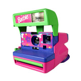A retro-style Barbie instant camera with a bright pink body, lime green top and flash housing, and a blue front panel decorated with small floral patterns. The Barbie logo is visible on the top left.