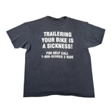 A faded black short-sleeve t-shirt with bold white text that reads 'TRAILERING YOUR BIKE IS A SICKNESS! FOR HELP CALL 1-800-SCARED 2 RIDE', laid flat on a white background.