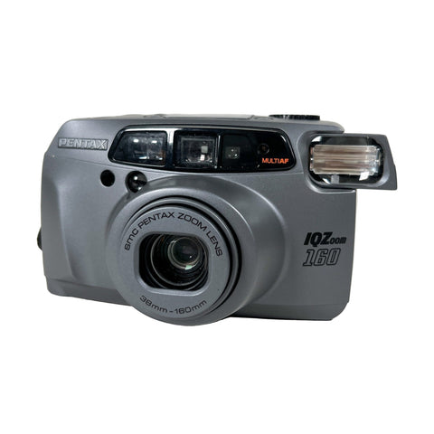 Gray Pentax camera with 'IQ Zoom' on a white background