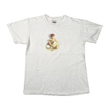 A white vintage graphic t-shirt laid flat on a light gray background. The shirt features a faded, low-contrast graphic of a seated figure with red hair and the word 'BREATHE' printed in a faint, light gray font behind it.