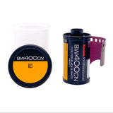 A roll of Kodak Professional BW400CN film with a purple film strip partially unrolled, shown next to its black and yellow cap and a white plastic spool on a white background.