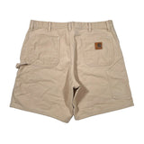 A pair of beige Carhartt cargo shorts shown from the back, featuring a brown leather brand patch on the right back pocket, photographed flat on a white background.