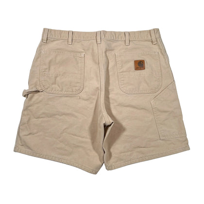 A pair of beige Carhartt cargo shorts shown from the back, featuring a brown leather brand patch on the right back pocket, photographed flat on a white background.