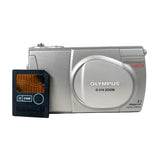 An Olympus D-S10 Zoom digital camera in silver, shown next to a black 64MB SD card on a plain white background.