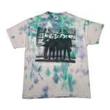 A vintage The Beatles tie-dye t-shirt featuring green and purple bleach-dye patterns over a light gray base, with a black graphic print of the band members on the front.