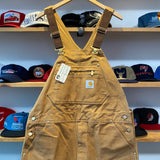 Brown overalls with a tag on a hanger against a background of various hats.