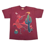 A vintage short-sleeve crewneck t-shirt in maroon, featuring a colorful graphic print of a Native American figure playing a flute next to a green cactus under a crescent moon.