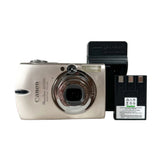 A Canon PowerShot SD250 camera in silver, shown with its black battery and charger on a light gray background.