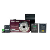 A Nikon Coolpix 10 digital camera in a metallic burgundy/maroon finish, shown with its black battery charger, a black Nikon battery pack, a black Kingston battery pack, and a small green-and-black adapter on a light gray background.