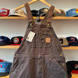 Brown denim overalls with a Carhartt logo on a hanger against a background of hats.