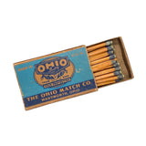 An open vintage matchbox from The Ohio Match Co. showing wooden matches with blue tips, set against a white textured background.