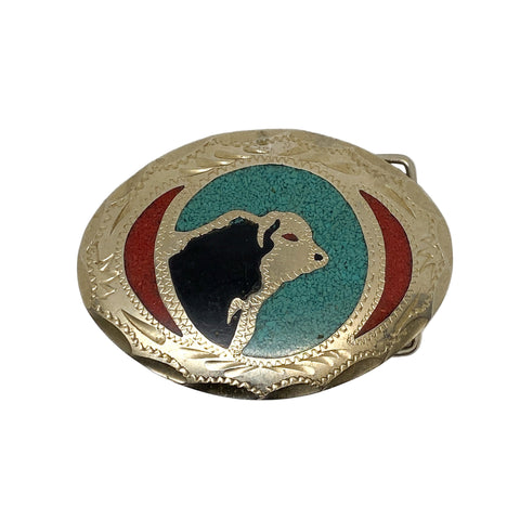 Belt buckle with black silhouette of a cow on a blue and red background, on a white surface