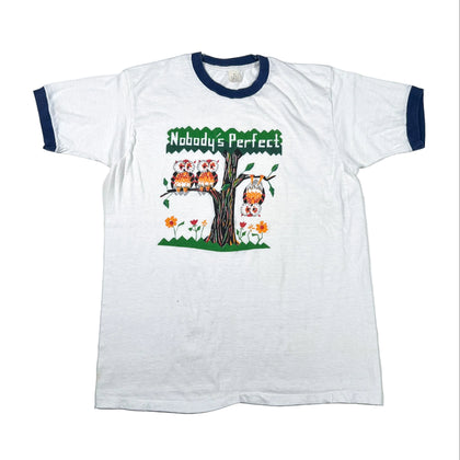 A white ringer t-shirt with navy blue collar and sleeve cuffs, featuring a colorful graphic of three owls perched on a tree branch with the text 'Nobody's Perfect' above them.