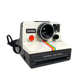 Vintage Polaroid One Step SX-70 Rainbow Stripe Instant Land Film Camera with a neckstrap, predominantly white with rainbow stripes and black details.