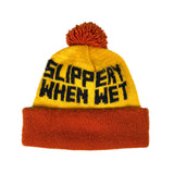 Yellow and orange beanie with 'SLIPPERY WHEN WET' text on a white background