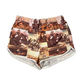 A pair of women's shorts featuring a vintage collage print of Western cowboy scenes in warm brown, beige, and orange tones, with a white ribbed inner lining visible at the leg openings, laid flat on a white background.