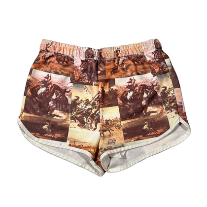 A pair of women's shorts featuring a vintage collage print of Western cowboy scenes in warm brown, beige, and orange tones, with a white ribbed inner lining visible at the leg openings, laid flat on a white background.