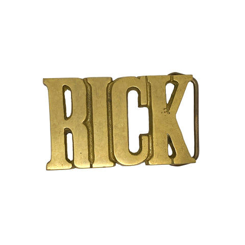 Gold belt buckle with 'RICK' engraved on a white background